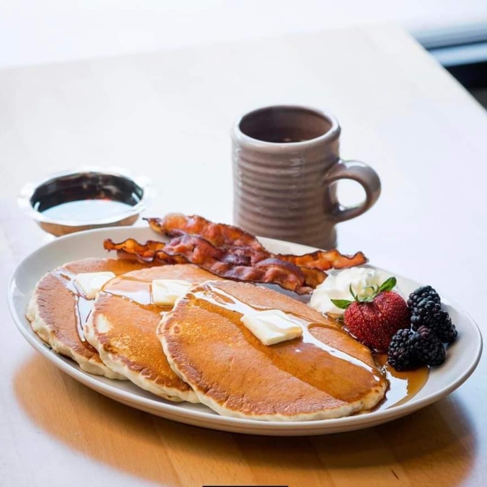 Pancakes with butter, syrup, bacon, whipped cream, strawberries, and blackberries, with coffee.
