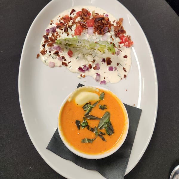 Wedge salad with bacon, blue cheese, and red onion, alongside a bowl of tomato soup.