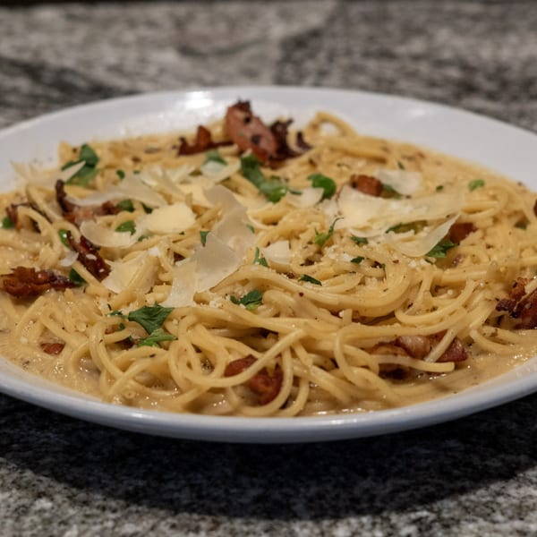 Creamy spaghetti carbonara with crispy bacon, fresh parsley, and shaved Parmesan cheese on a white plate.