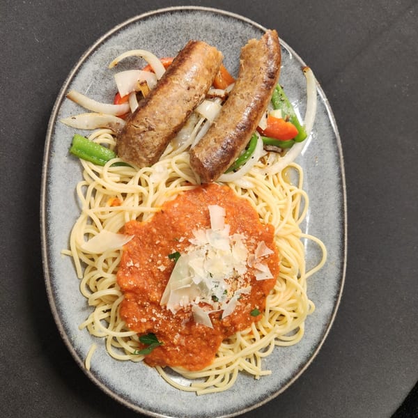 Spaghetti with red sauce and parmesan, topped with two sausages and sautéed onions and peppers.