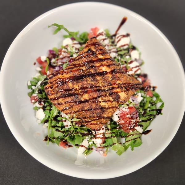 Grilled salmon with balsamic glaze on a bed of arugula, feta, and tomatoes in a white bowl.