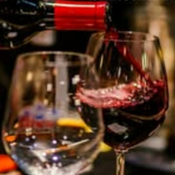 Red wine pouring from a bottle into a glass, with another empty glass beside it.