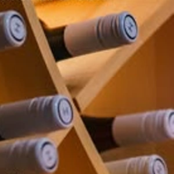 Wine bottles with white labels and dark caps stored in a wooden wine rack.